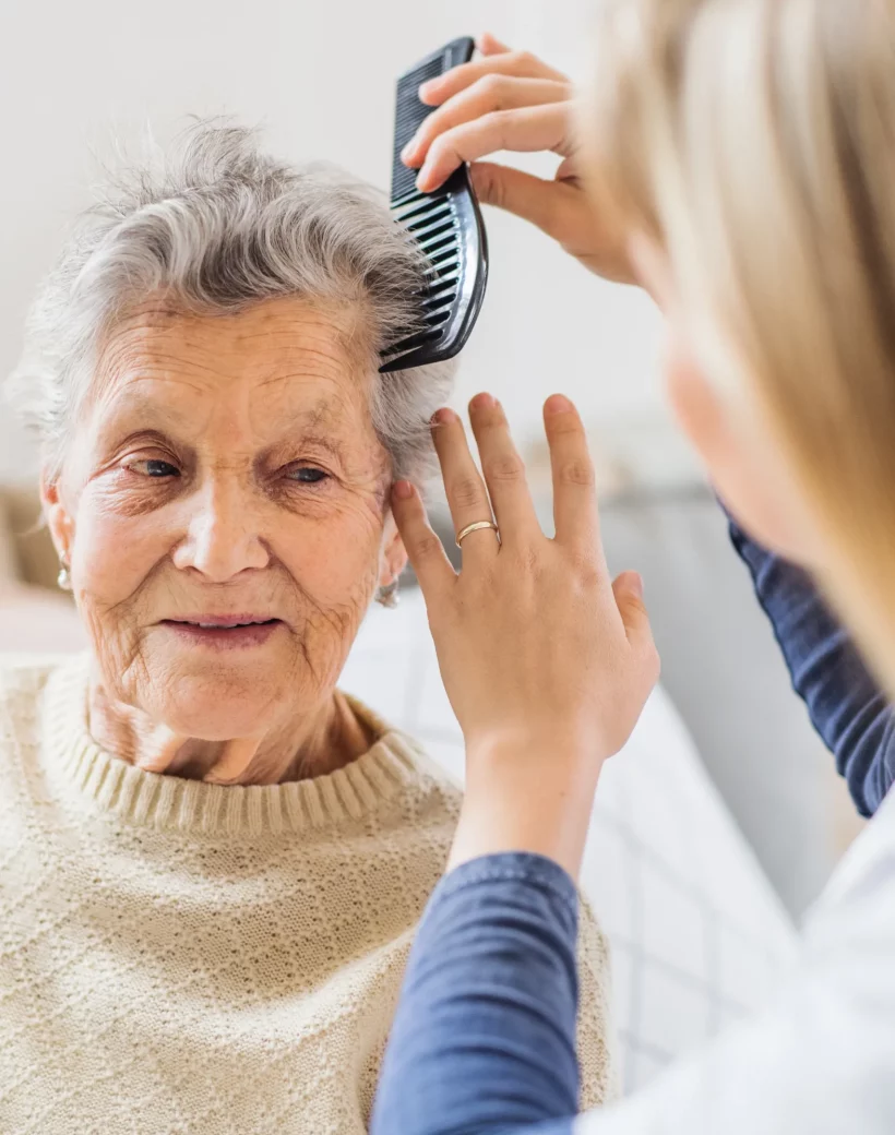 a-health-visitor-combing-hair-of-senior-woman-at-h-2021-08-26-12-09-30-utc