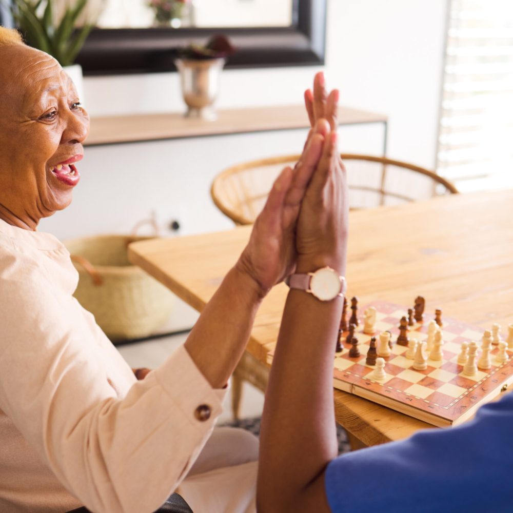 Black people, nurse and high five in elderly care for chess, fun or social activity or game togethe.